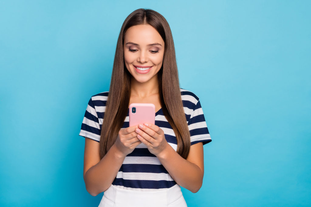 Photo of beautiful cheerful lady hold telephone hands reading, email check blog comments reactions followers wear striped t-shirt white skirt isolated blue color background